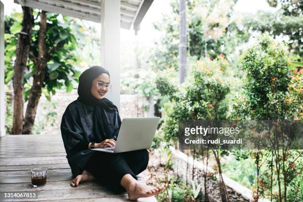 junge hijab frau sitzt auf dem boden auf hinterhof - indonesia women stock-fotos und bilder