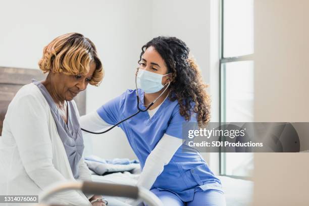 senior woman waits patiently as nurse checks heart and lungs - nurse listening to patient stock pictures, royalty-free photos & images