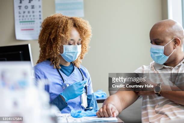 nurse gives vaccinations to patients at covid-19 clinic - 50 year old male patient stock pictures, royalty-free photos & images