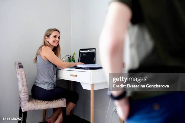 a young woman sits working at home with a laptop, and her 11-year-old son looks at her and distracts her from work - distracts stock pictures, royalty-free photos & images