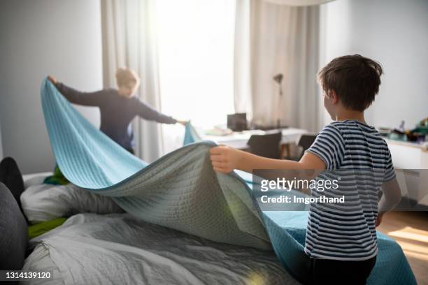 niños haciendo cama en su habitación antes de las lecciones en línea - montar fotografías e imágenes de stock