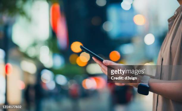close up mid-section of young asian woman using smartphone in downtown city street at night, against illuminated and multi-coloured city street light. technology in everyday life - asian and indian ethnicities smartwatch phone stock pictures, royalty-free photos & images