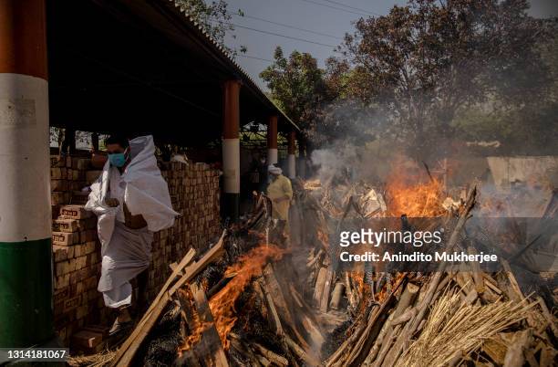 Priest who helps performing last rites, runs to avoid the heat from the multiple burning funeral pyres of patients who died of the Covid-19...