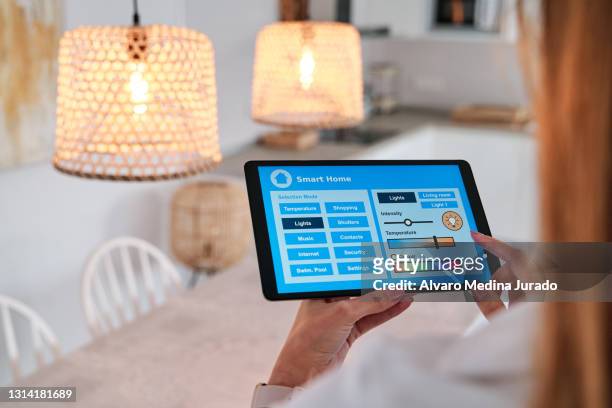 woman using an app on her smartphone to control the lighting in her smart home - smartes stock-fotos und bilder