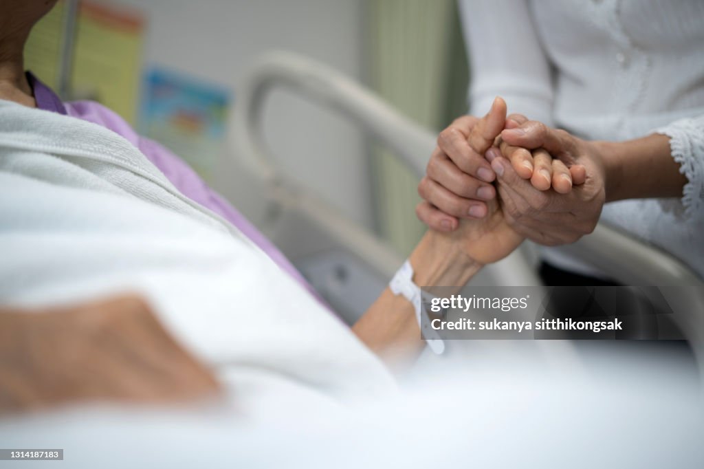 Shot of daughter encourage her mother and holding the mother's hand to sleep on the bed ​in hospital.