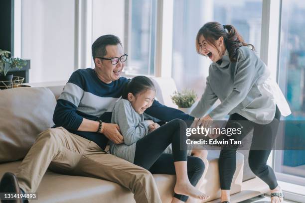 asiatische chinesische 2 eltern kitzeln spielen mit ihren kindern zu hause im wohnzimmer kuscheln auf dem sofa - living room young couple stock-fotos und bilder