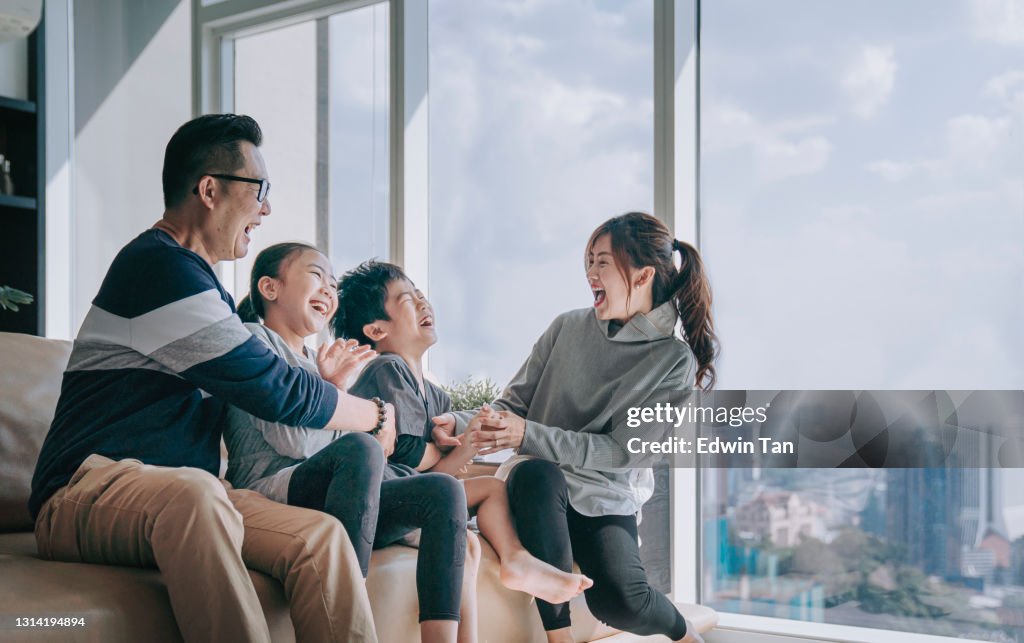Asian chinese 2 parent tickling playing with their children at home in living room cuddle on sofa