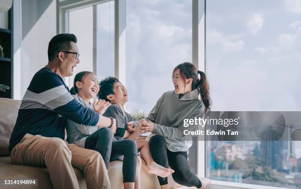 asian chinese 2 parent tickling playing with their children at home in living room cuddle on sofa - asiático imagens e fotografias de stock