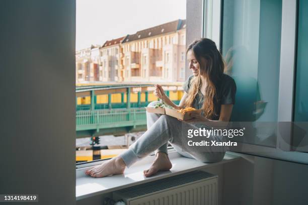 woman with take out salad at home on the windowsill - window sill stock pictures, royalty-free photos & images