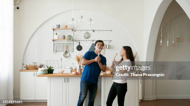 happy young couple dancing in the kitchen while preparing breakfast at home - couple dancing at home stockfoto's en -beelden
