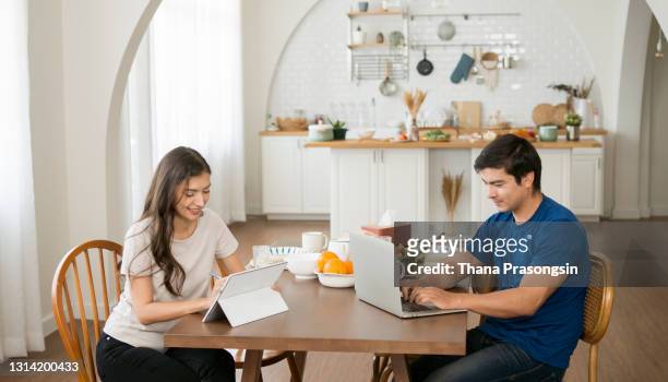 boyfriend and girlfriend smiling while looking at laptop on table - mid adult couple stockfoto's en -beelden
