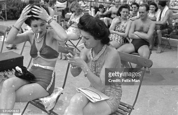 Two young women smoke and fix their hair next to Roehampton's outdoor swimming pool, South London, 10th July 1943. Original Publication : Picture...