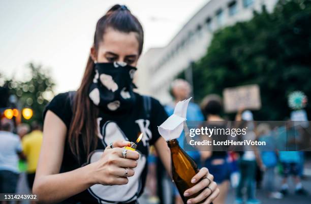 female protester lights molotov cocktail - cocktail molotov imagens e fotografias de stock