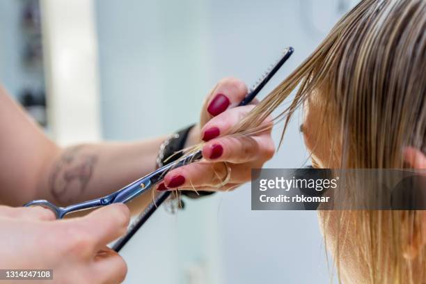 hands of a professional hairdresser scissors the bangs of wet hair of a blonde woman. fashionable hairstyle design in a beauty salon. small female business - fringe stock-fotos und bilder