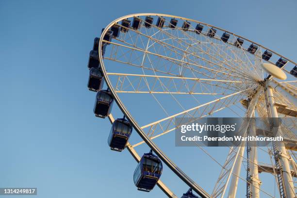 low angle view of white structure and blue cabin of ferris wheel with background of clear blue sunny sky. - ferris wheel fotografías e imágenes de stock