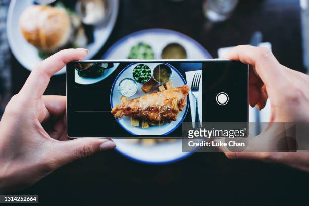 kvinna fotograferar fish and chips i en restaurang med en smartphone - automatiskt postproduktionsfilter bildbanksfoton och bilder