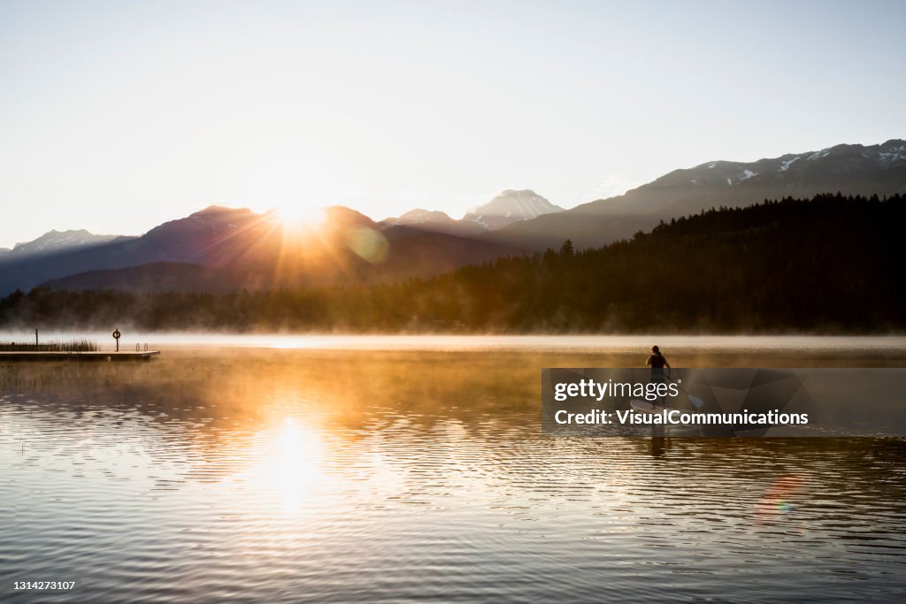 Frau Paddeln auf ruhigen See in Whistler bei Sonnenaufgang.