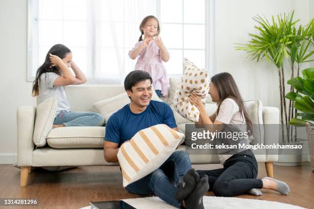 playful parents engaged in pillow fight with little daughter - spending stock pictures, royalty-free photos & images