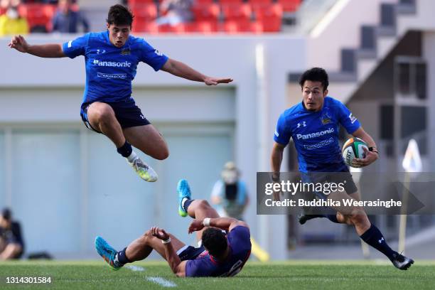 Kenki Fukuoka of Panasonic Wild Knights breaks through a tackle of Siosaia Fifita of Kintetsu Liners as Dylan Riley of Panasonic Wild Knights leaps...