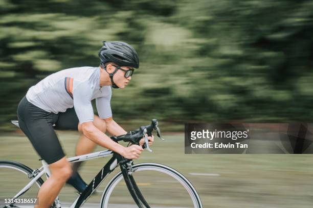 zijaanzicht aziatische chinese professionele fietser atleet sportman sprinten fietsen in de regen in landelijk gebied - forward athlete stockfoto's en -beelden