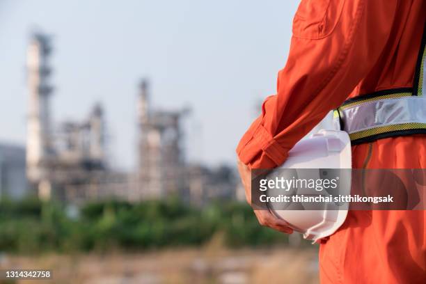 rear view of engineer man in suite stand , holding white safety helmet and blur refinery oil background. - power occupation stock pictures, royalty-free photos & images