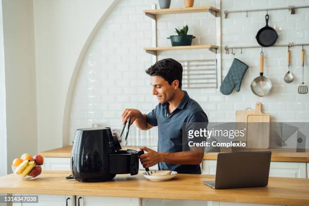 mann mit luftfritteuse und laptop in der küche - haushaltsmaschine stock-fotos und bilder