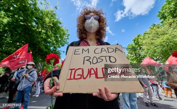 Mask-clad participant in the parade holds a red carnation and sign quoting "Em Cada Rostro Igualdade" while walking through Avenida da Liberdade to...