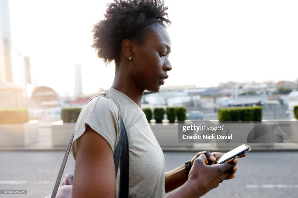 A young women checking her phone as she walks down the street in the city