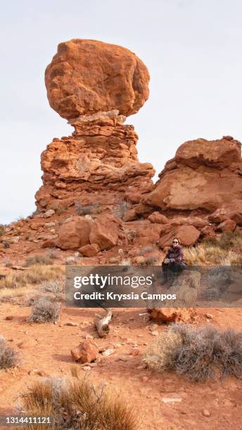 woman sitting in front of balanced rock, arches national park, utah - double arch foto e immagini stock