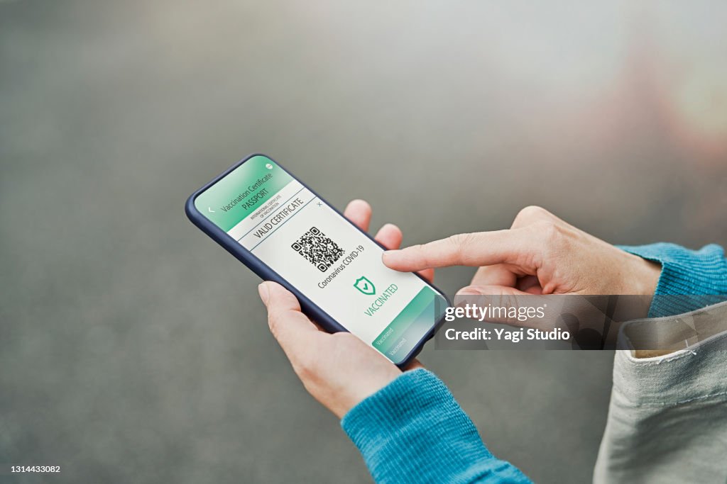 Mid adult woman using a Digital vaccine passport with smart phone in outdoor.