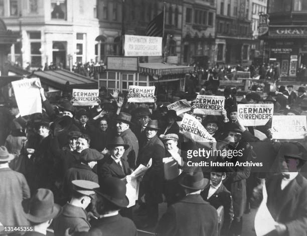 Despite government reports to the contrary, a Times Square crowd excitedly holds up copies of The Evening Mail newspaper touting a headline that...