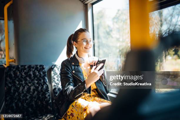 ung kvinna skrattar medan hon smsar och lyssnar på musik på en buss - bus bildbanksfoton och bilder