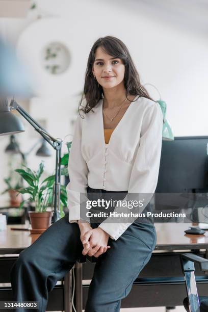 portrait of businesswoman sitting on computer desk - leanincollection working women stockfoto's en -beelden