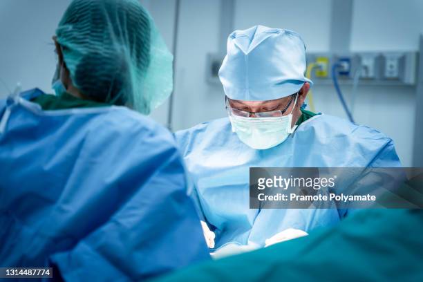 close up face of surgeons working surgical stitches are in progress during operation. professional medical doctors performing surgery and assistant hands out instruments inside modern operating room - chirurgie stockfoto's en -beelden