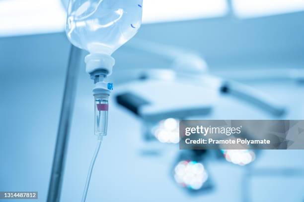 saline syringe pump with blurred background.intravenous fluid used in the operating room while doctor perform surgery. surgical lamp in background with red highlight. medical concept. - iv drip stockfoto's en -beelden