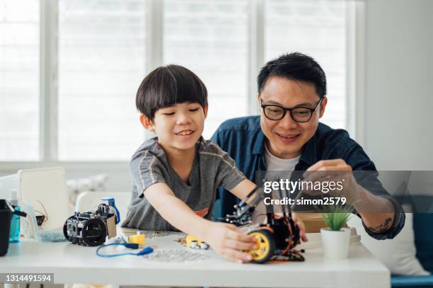 vrolijke kleine zoon en zijn vader die bij de lijst zitten en hun robots bij woonkamer testen - malaysia father and son stockfoto's en -beelden