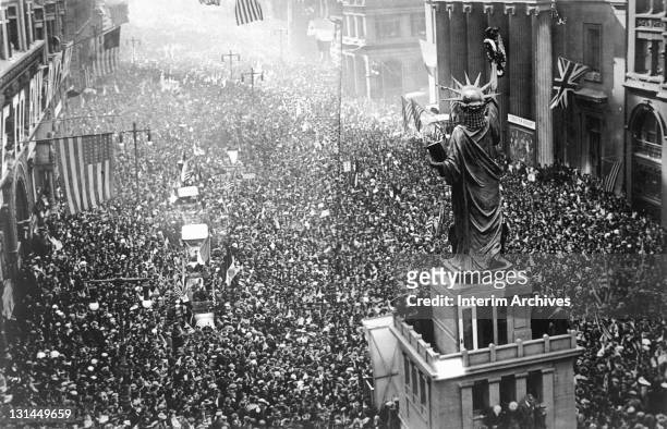Crowd of thousands massed on Broad Street near a replica of the Statue of Liberty, to cheer as news of the armistice was announced to the public,...