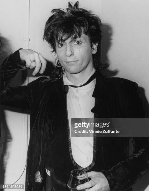 American singer-songwriter and guitarist Johnny Thunders wearing a dark velvet jacket and a white shirt, holding a brandy glass, at the Limelight, a...