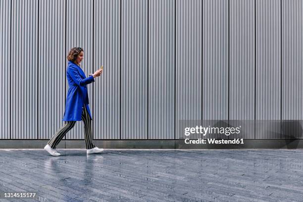 female professional using smart phone while walking on footpath - business woman side stockfoto's en -beelden