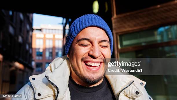 young man wearing knit hat laughing during sunny day - man laughing photos et images de collection