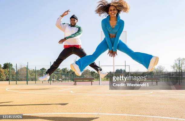 confident male and female friends jumping while dancing on basketball court - legs apart imagens e fotografias de stock