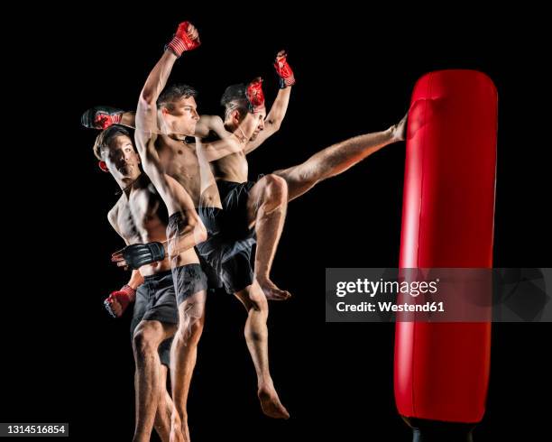 young shirtless male martial arts athlete kicking punching bag over black background - martial arts background stock pictures, royalty-free photos & images