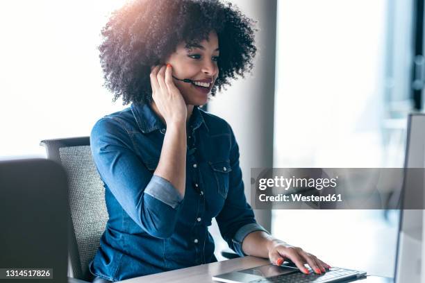 smiling female customer service representative talking through headphones at desk in office - helpdesk stock pictures, royalty-free photos & images