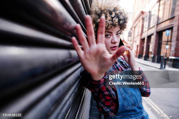 woman showing stop gesture while talking on mobile phone - hand stop stock-fotos und bilder