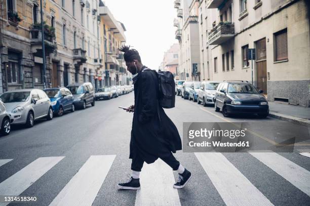 fashionable man using mobile phone while crossing road in city - paso de cebra fotografías e imágenes de stock