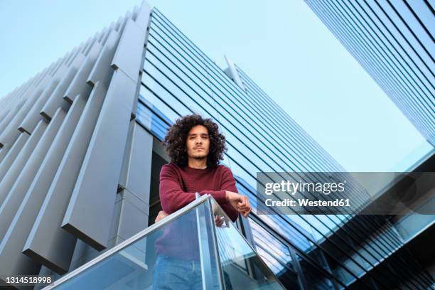 caucasian young man leaning on railing while modern office building in background - low angle portrait stock pictures, royalty-free photos & images