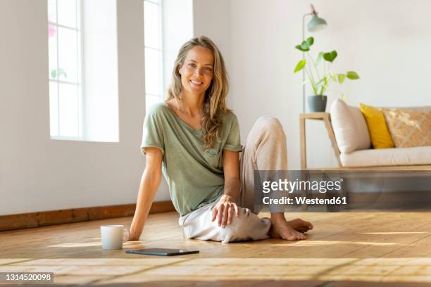 happy woman sitting on floor by digital tablet and mug at home - happy ipad beautiful stockfoto's en -beelden