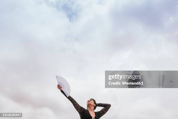 female dancer with hand fan performing flamenco under cloudy sky - fächer stock-fotos und bilder