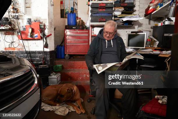 senior male auto mechanic reading newspaper while sitting in garage - man in car reading newspaper stock pictures, royalty-free photos & images
