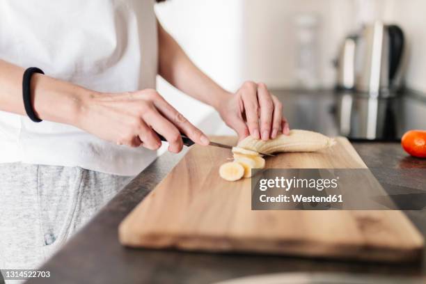 mature woman cutting banana on board in kitchen - banana woman stock pictures, royalty-free photos & images